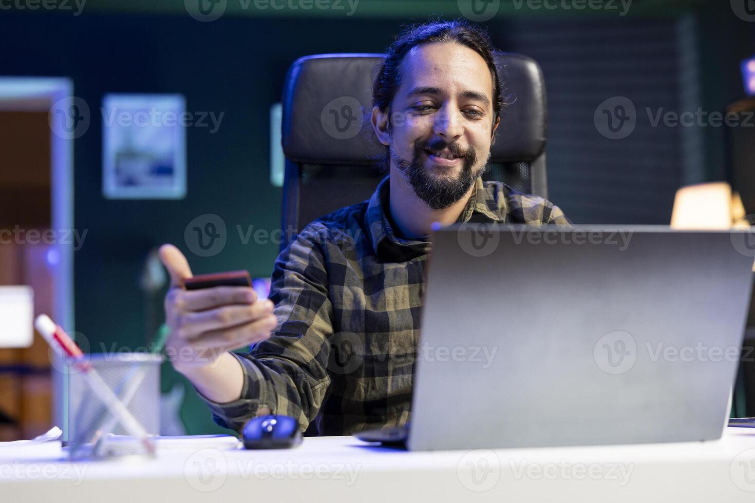 Happy bearded man holding and using his credit card for online shopping. Smiling male individual typing card information on laptop for e commerce banking, performing cashless payments. photo