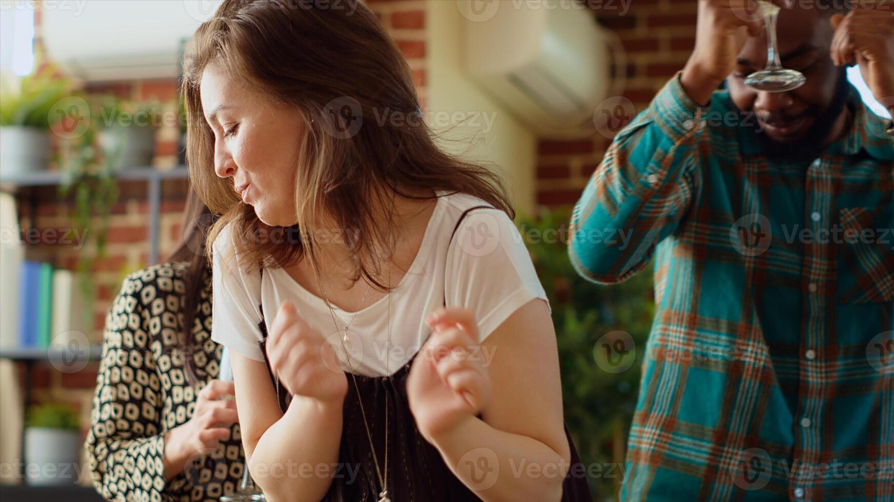 Guests at home party doing dance moves on pop music in living room, holding alcoholic beverages in hand. Group of people dancing on energetic beats during weekend hangout, shaking hips photo