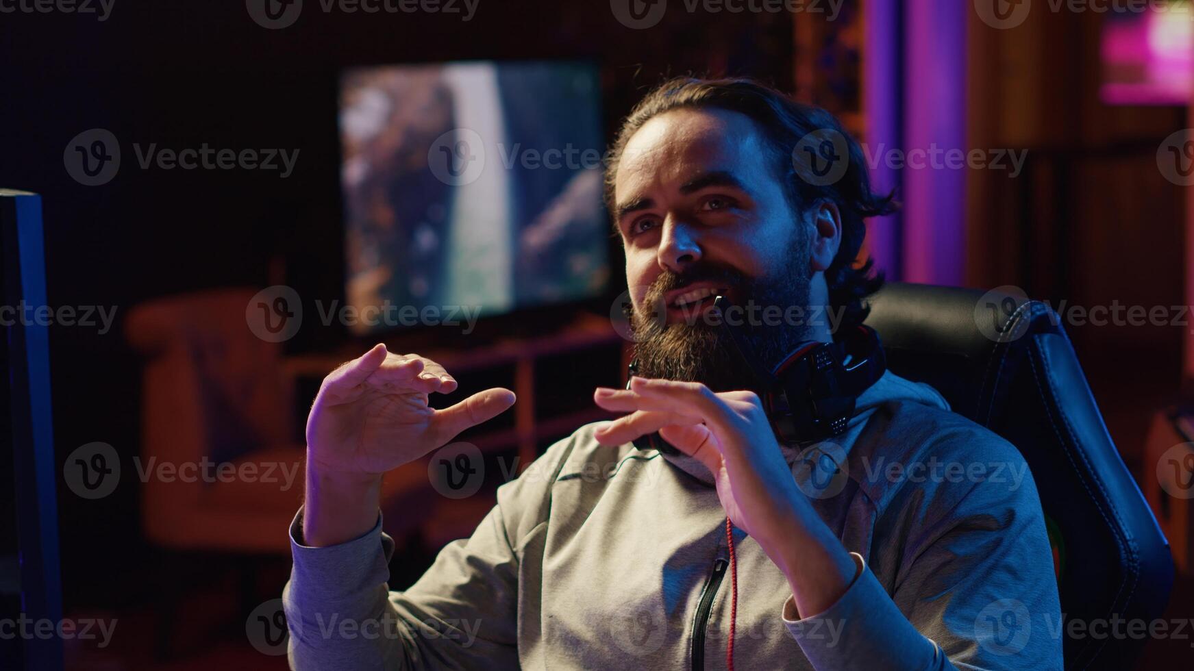 Content creator playing videogames live while chatting with online audience from RGB lit studio. Professional gamer streaming multiplayer game while discussing his strategies with fans photo