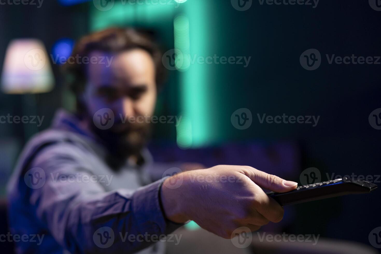 Focus on remote control used by man in blurry background switching channels on television screen. Close up of device used by person to scroll through streaming content, picking movie photo