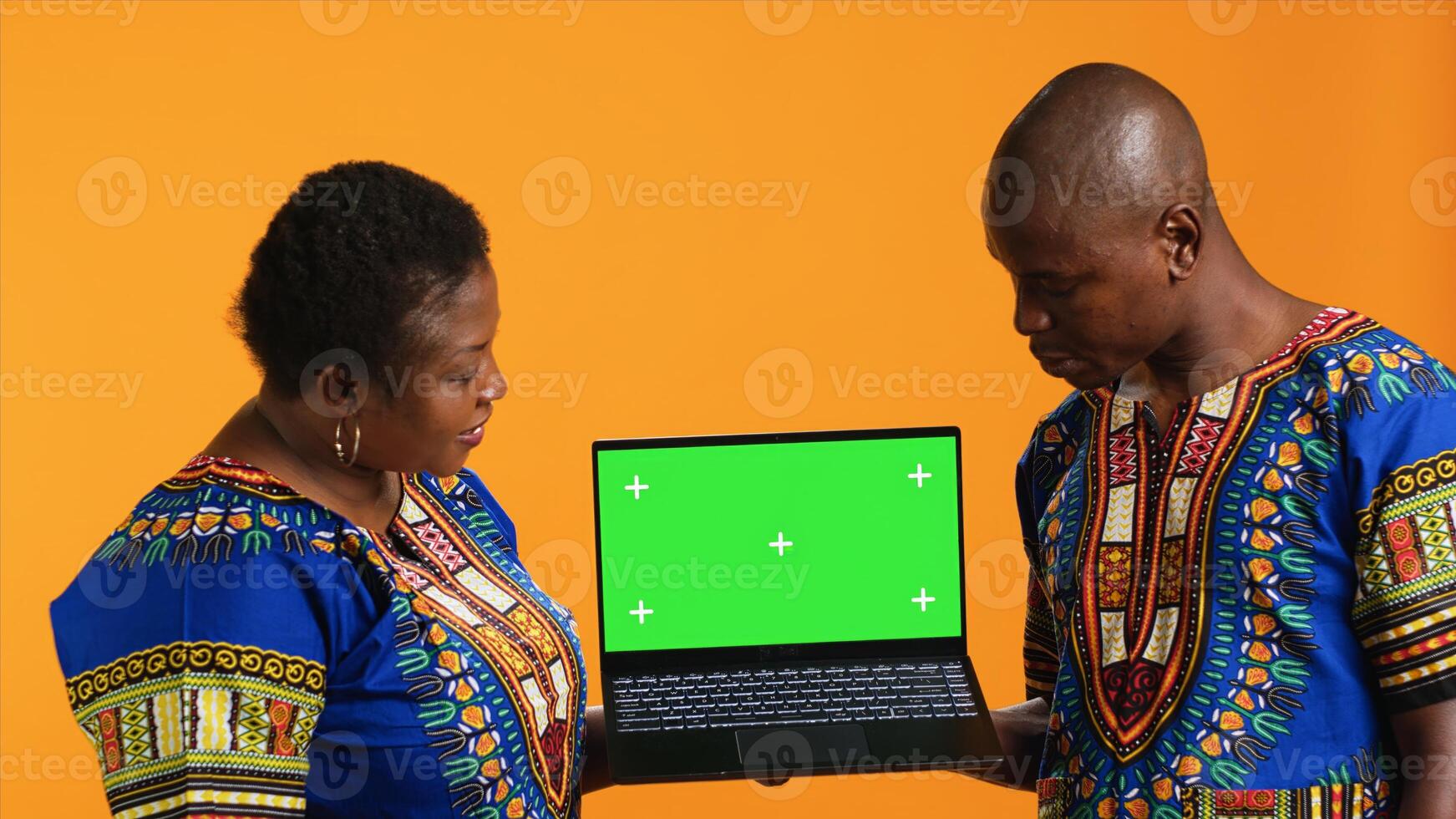 Ethnic people pointing to laptop with greenscreen layout, posing on camera with wireless pc showing blank copyspace display. Man and woman looking at isolated chromakey template in studio. photo
