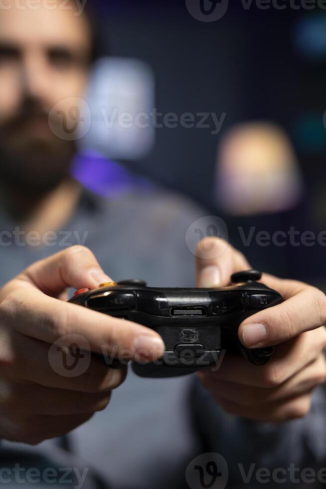 Focus shot on controller held by man defeating enemies while playing videogames on gaming console with teammates. Player in blurry background using gamepad to participate in esports game photo