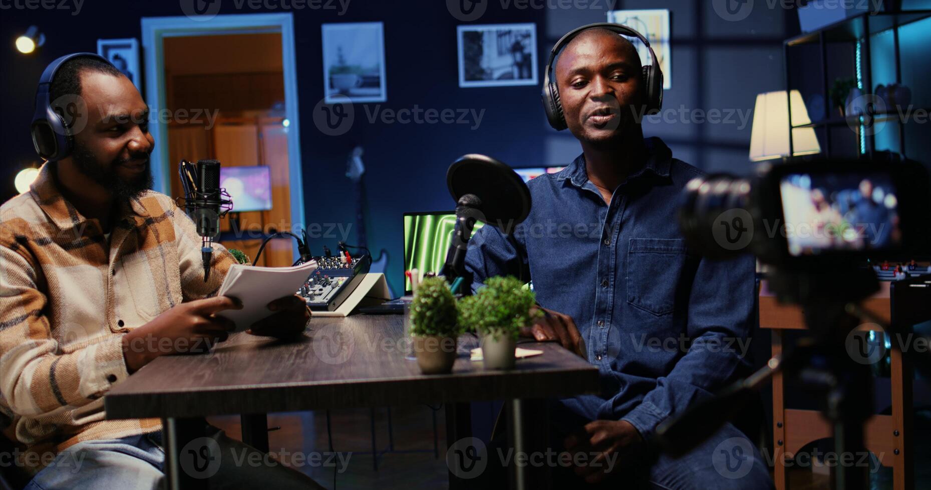 African american host engaging in entertaining discussion with man during livestream in apartment studio, making him laugh. Presenter uses high tech filming gear to produce comedy podcast photo