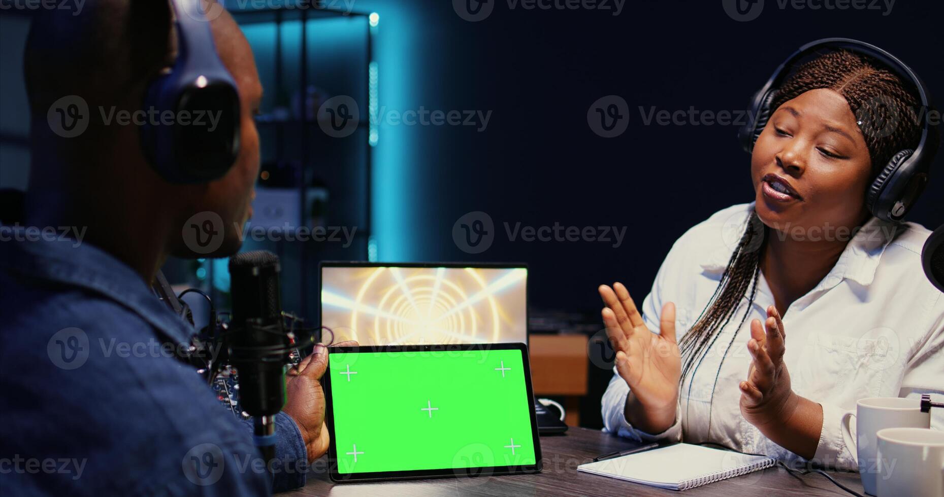 Woman invited to podcast watching internet clips on green screen tablet with host in studio, discussing content. African american guest reacting to videos on mockup device during online comedy show photo
