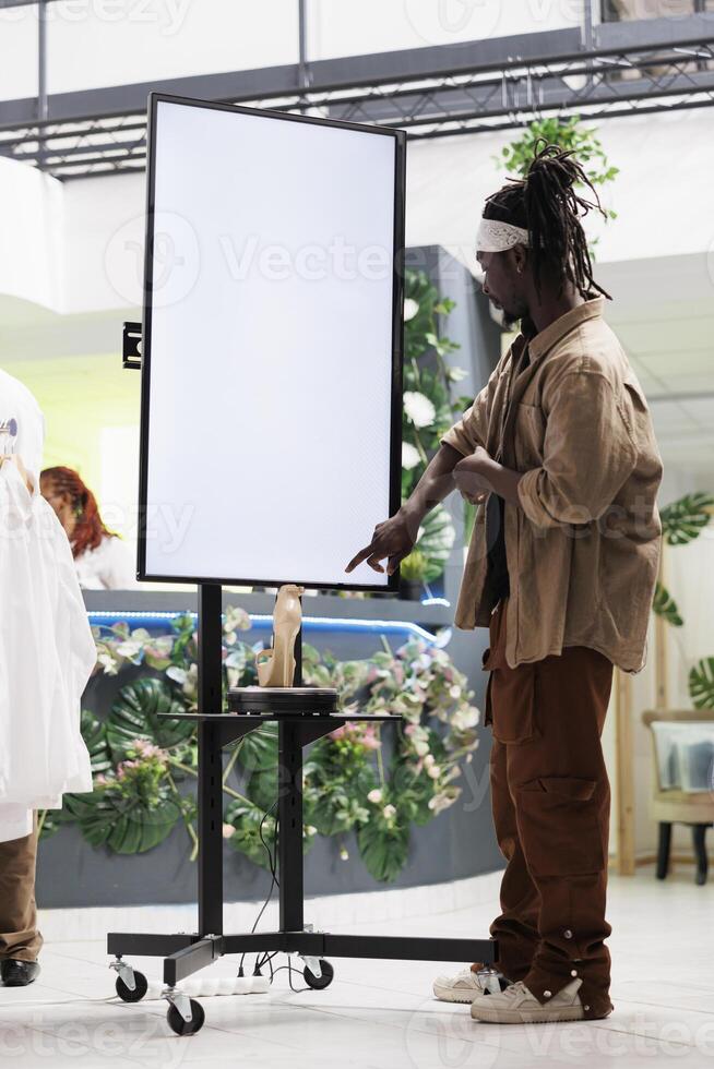 African american customer checking shoes advertisement on smart display board in boutique. Clothing store client reading information on whiteboard showcasing female stiletto brand collection photo