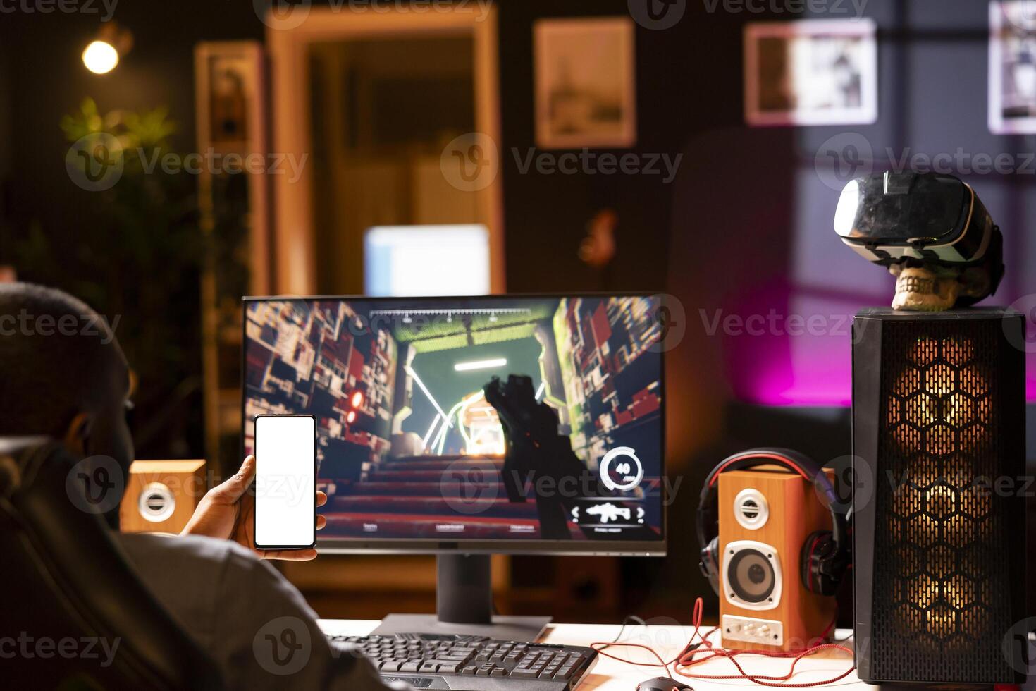 Isolated screen smartphone held by player competing in online multiplayer videogame at home. Mockup mobile phone utilized by person playing on gaming PC in neon illuminated apartment photo