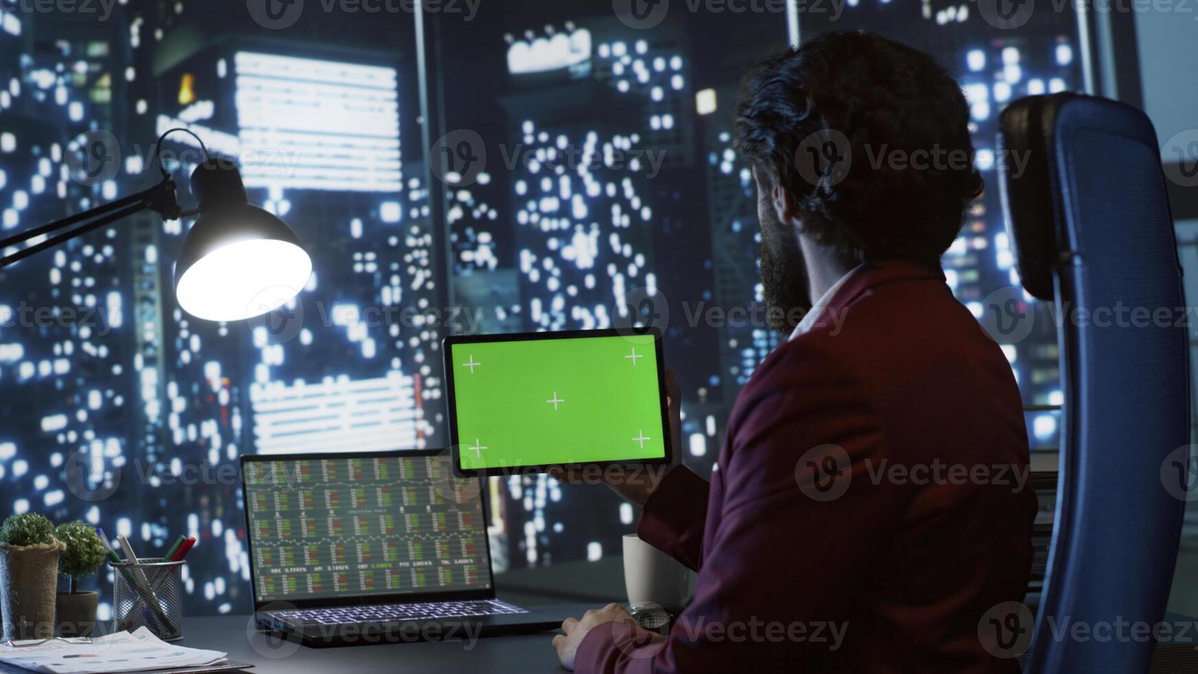 Private equity associate uses greenscreen display on tablet, sitting at workstation inside skyscraper. Influential chairman looks at gadget with blank copyspace template screen, legal work. photo