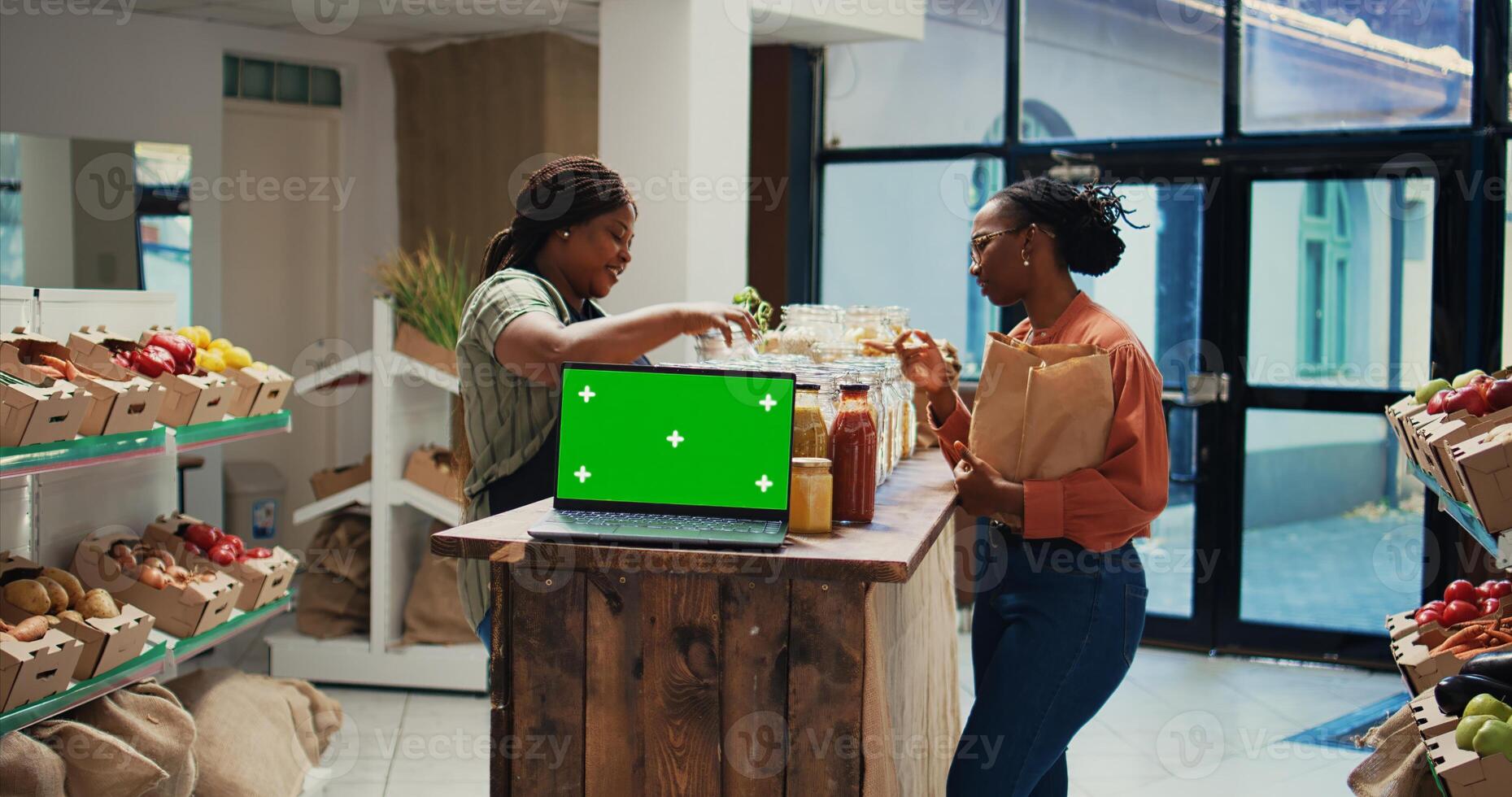Vendor presenting eco goods on shelves next to greenscreen, recommends natural bulk products in organic shop. Laptop placed on stall running isolated chromakey layout template. Tripod shot. photo