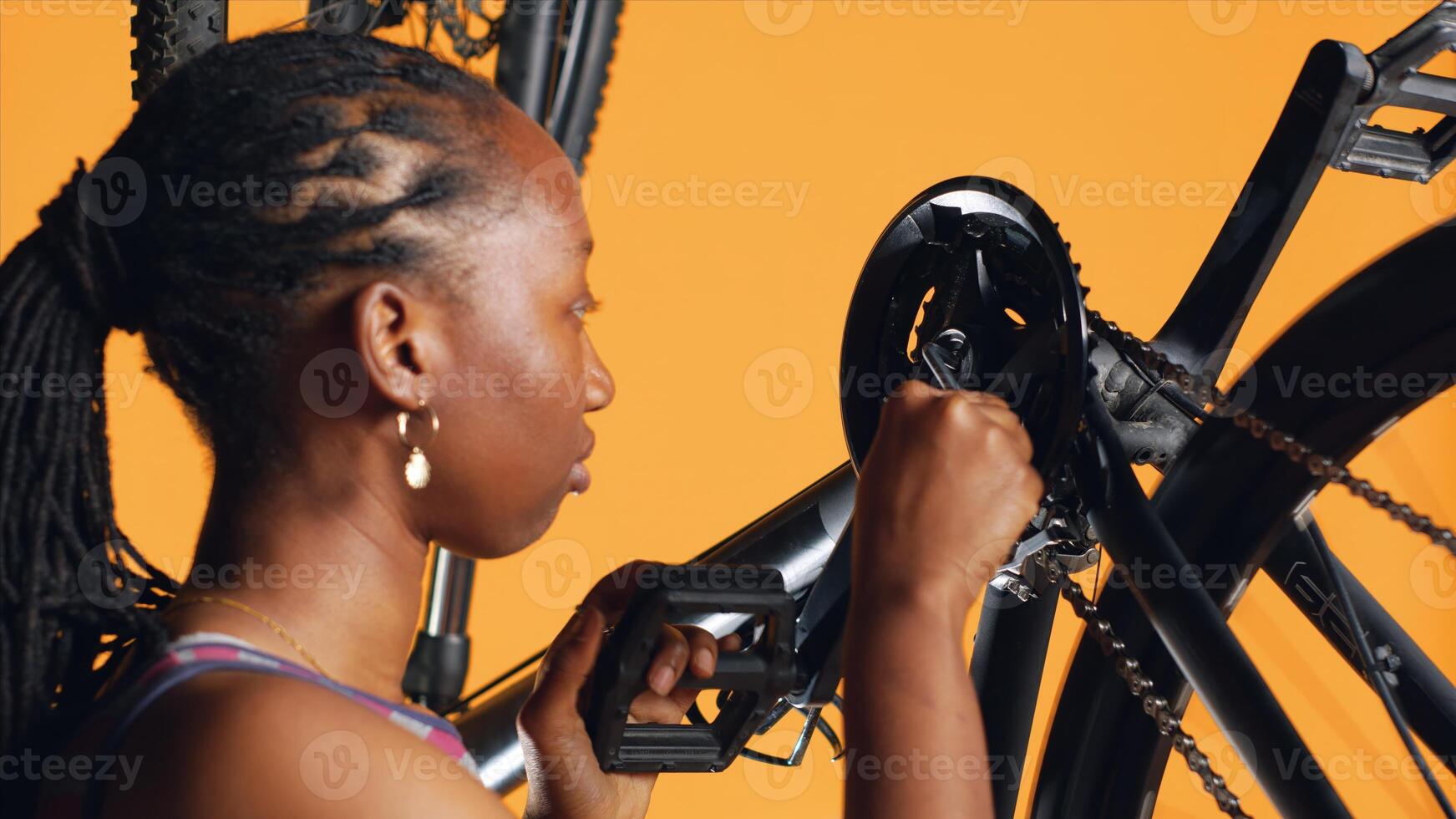 African american woman pushing pedals to spin bike wheel, inspecting it, using screwdriver and hex socket wrench to fix it, close up shot. Riding hobbyist testing bicycle crank arm and chain rings photo