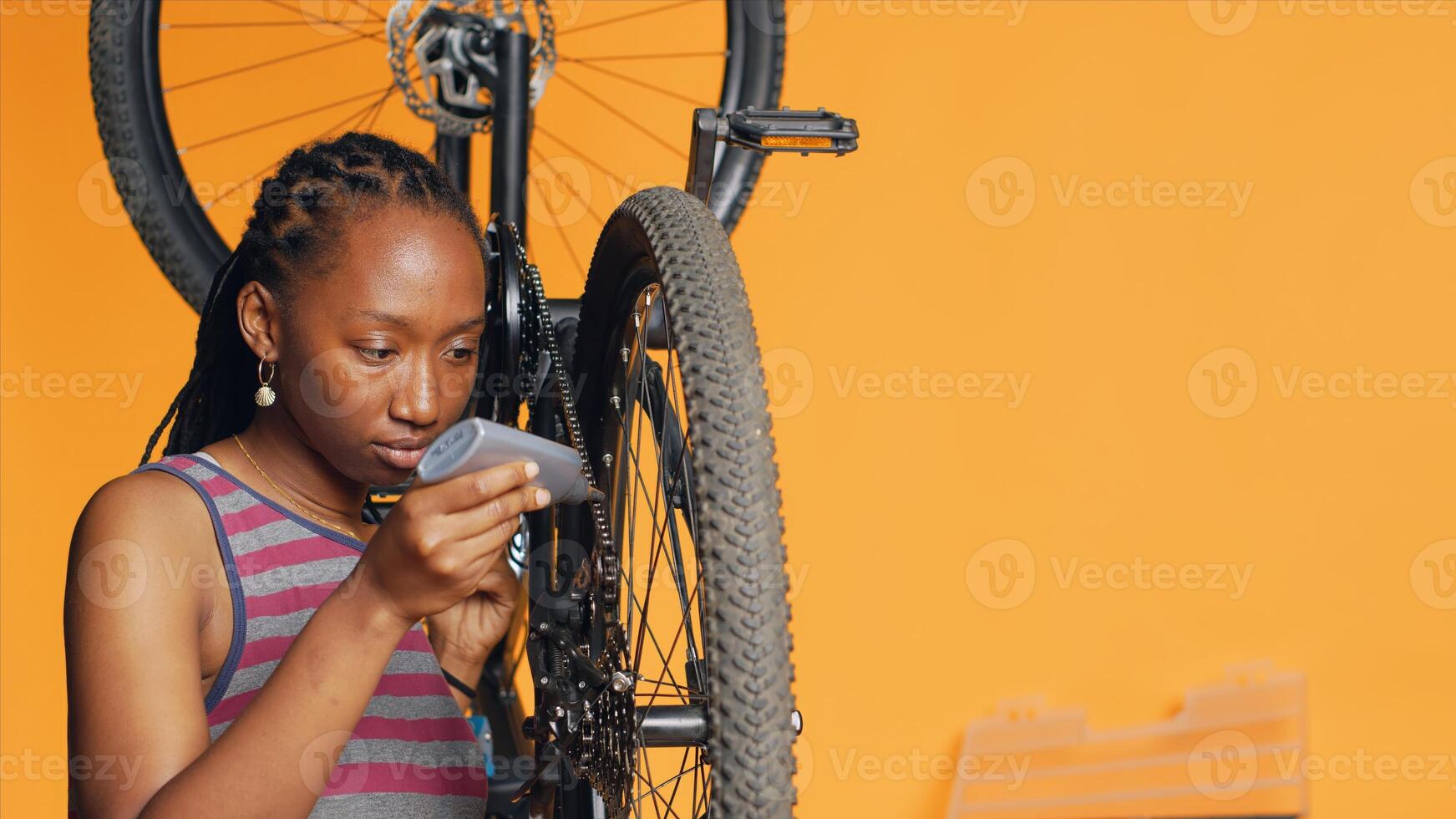 African american woman using specialized glue to repair broken bicycle chain, studio background. Skilled engineer applying adhesive on bike components during maintenance process, camera A photo