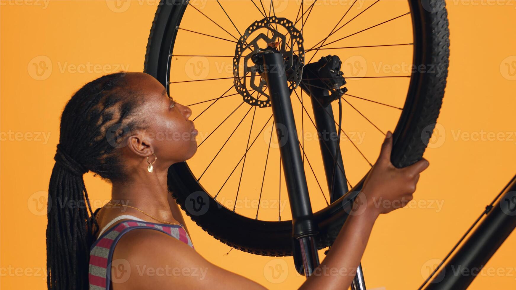 Woman detaching bicycle wheel and adjusting handlebar in studio background repair shop. Cycling hobbyist disassembling bike tire, repairing components with professional equipment, camera A photo