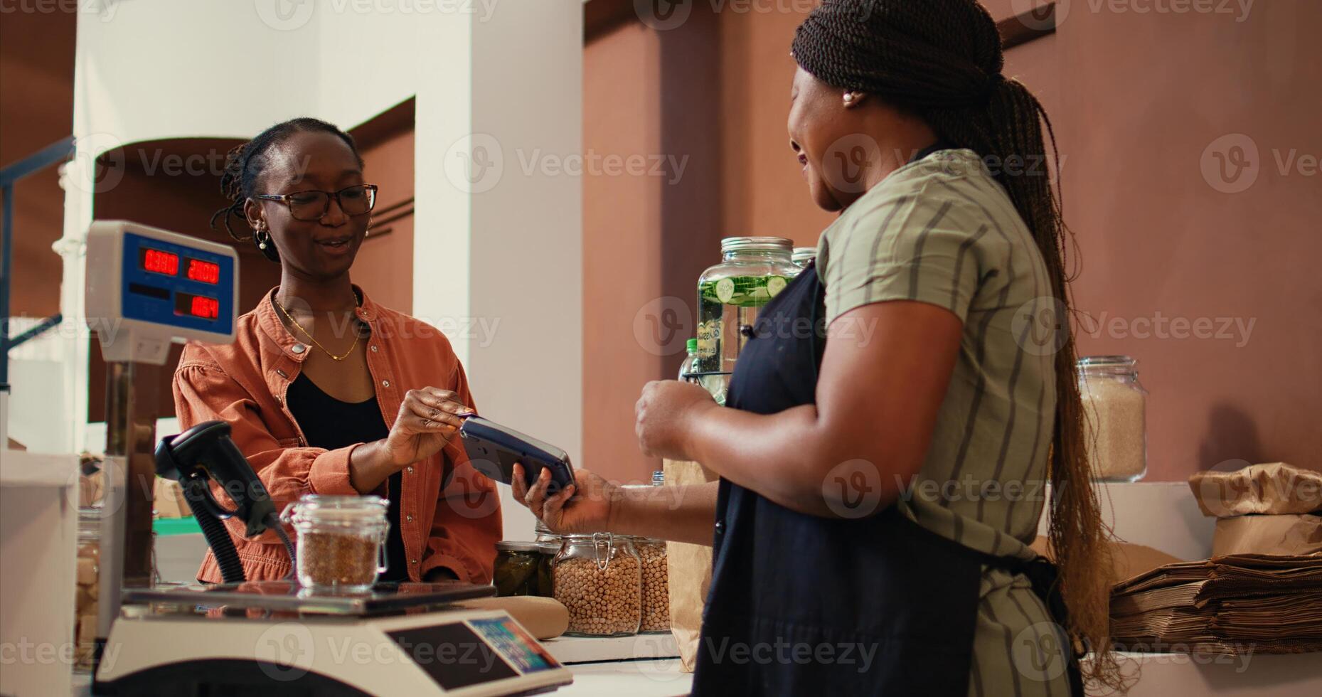 Woman using card payment at pos to buy fresh produce, choosing ripe colorful fruits and vegetables for healthy nutrition. Client paying for organic locally grown goods at checkout. Handheld shot. photo