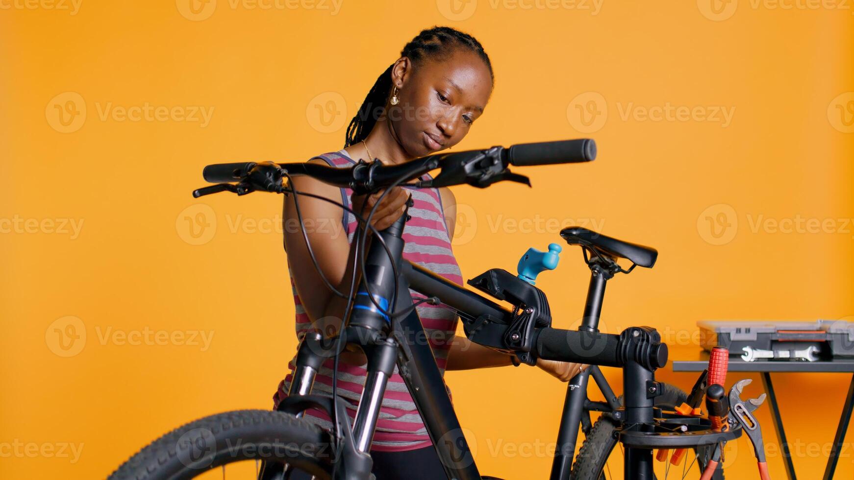 BIPOC mechanic setting up bike repair stand, using it to adjust handlebar and fix broken wheels, studio background. Professional placing bicycle on workstand in tight grip to inspect it, camera B photo