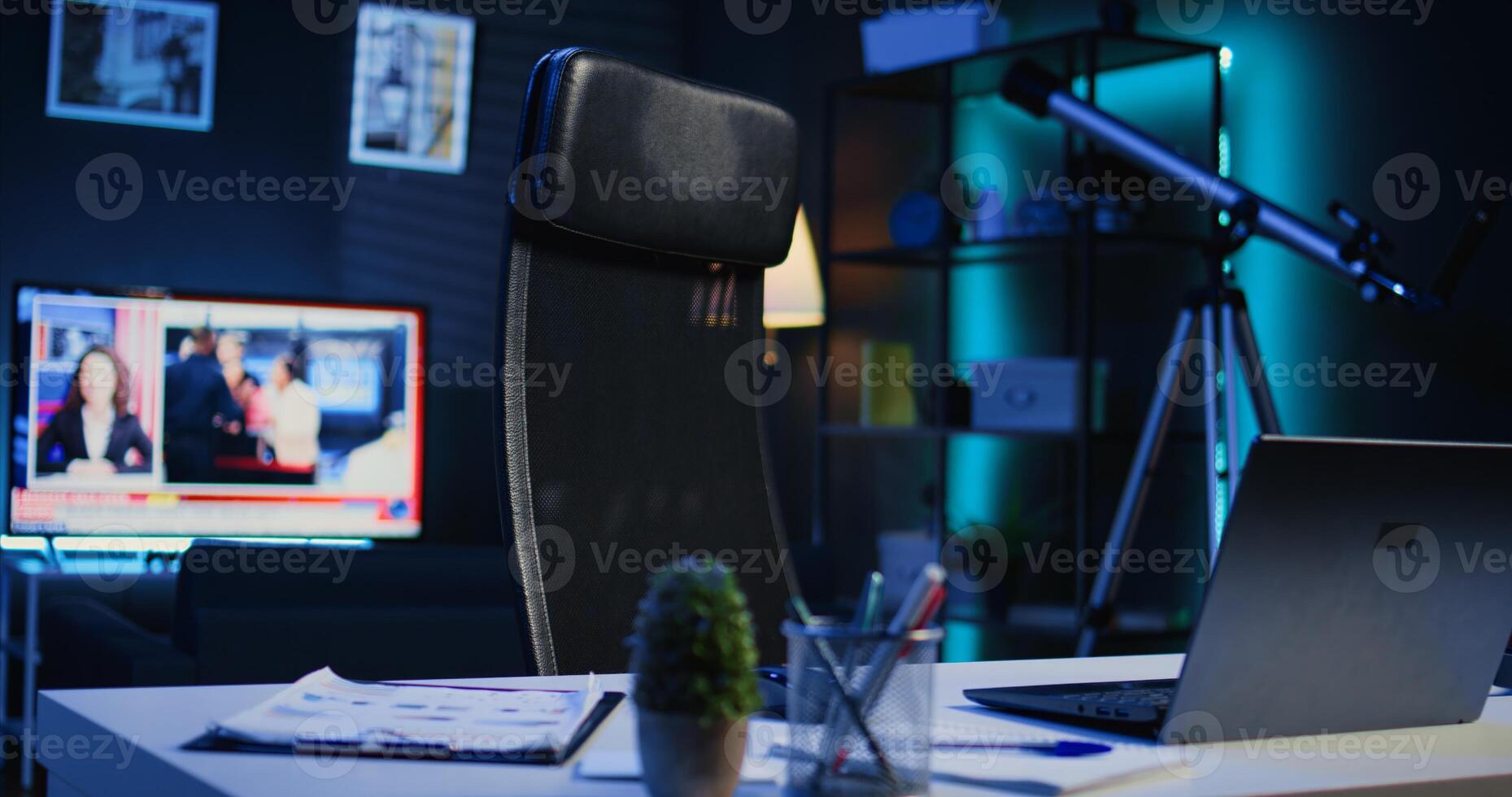 Apartment illuminated by RGB lights with office desk in front of smart TV displaying news program broadcasting. Laptop, mini house plants and headphones on table in empty room, camera B close up shot photo