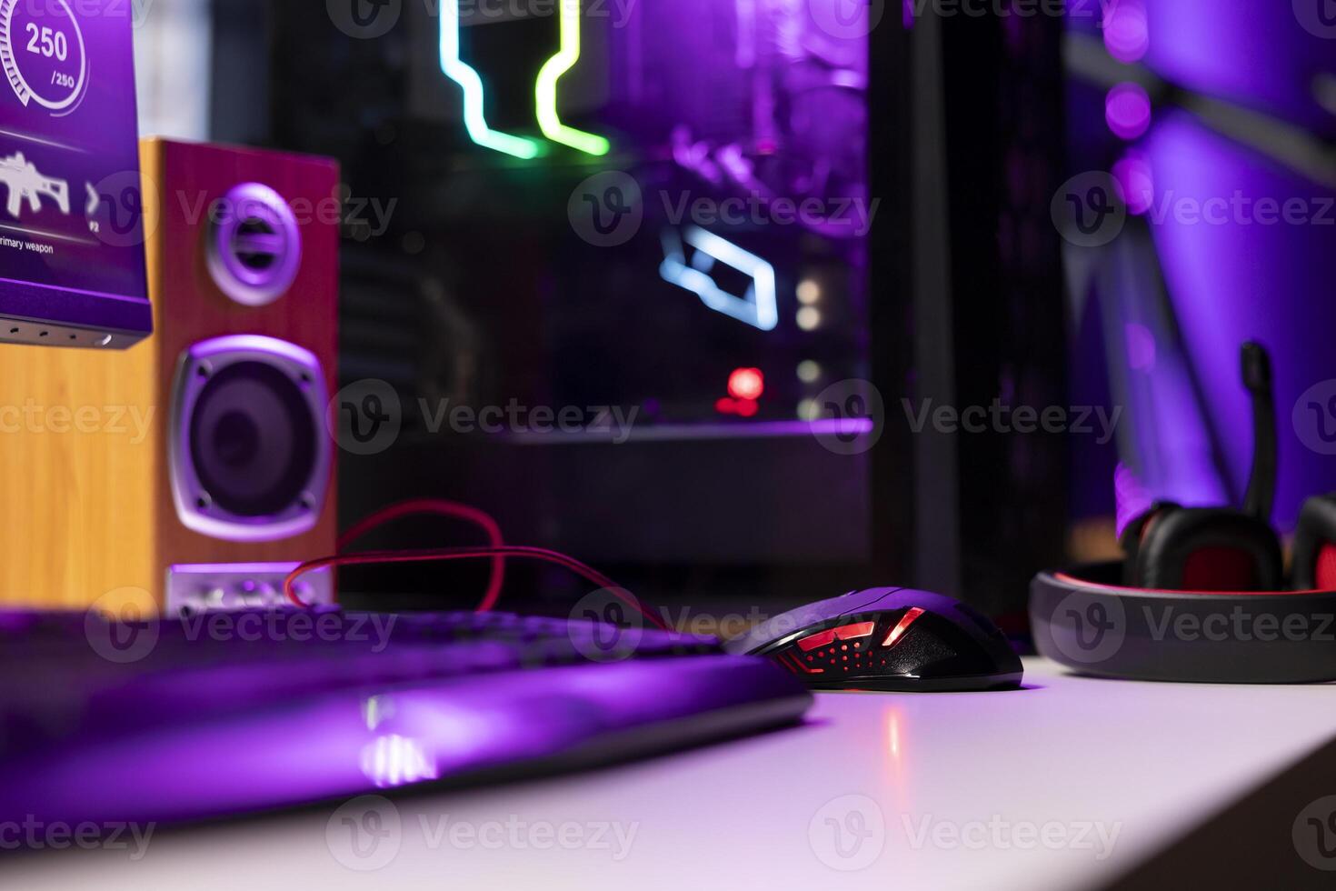 Neon lit components on opened gaming PC device next to keyboard, speakers, wired mouse and headphones in empty apartment. Computer in home with colorful gpu and cpu parts, close up shot photo