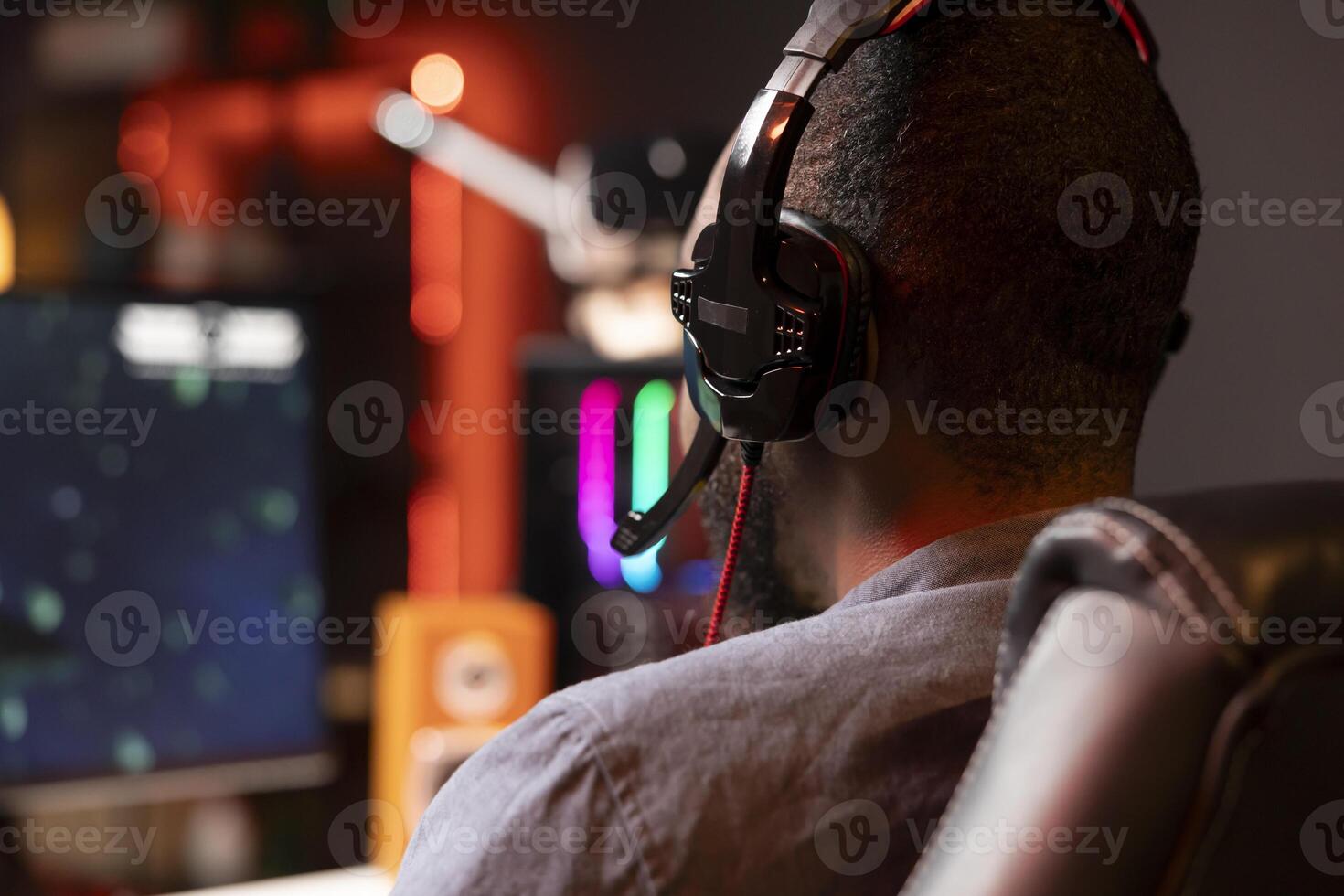 Player using headphones to discuss with mates while playing online videogame on gaming PC monitor. Man enjoying coop game with friends on computer display, chatting on internet late at night photo