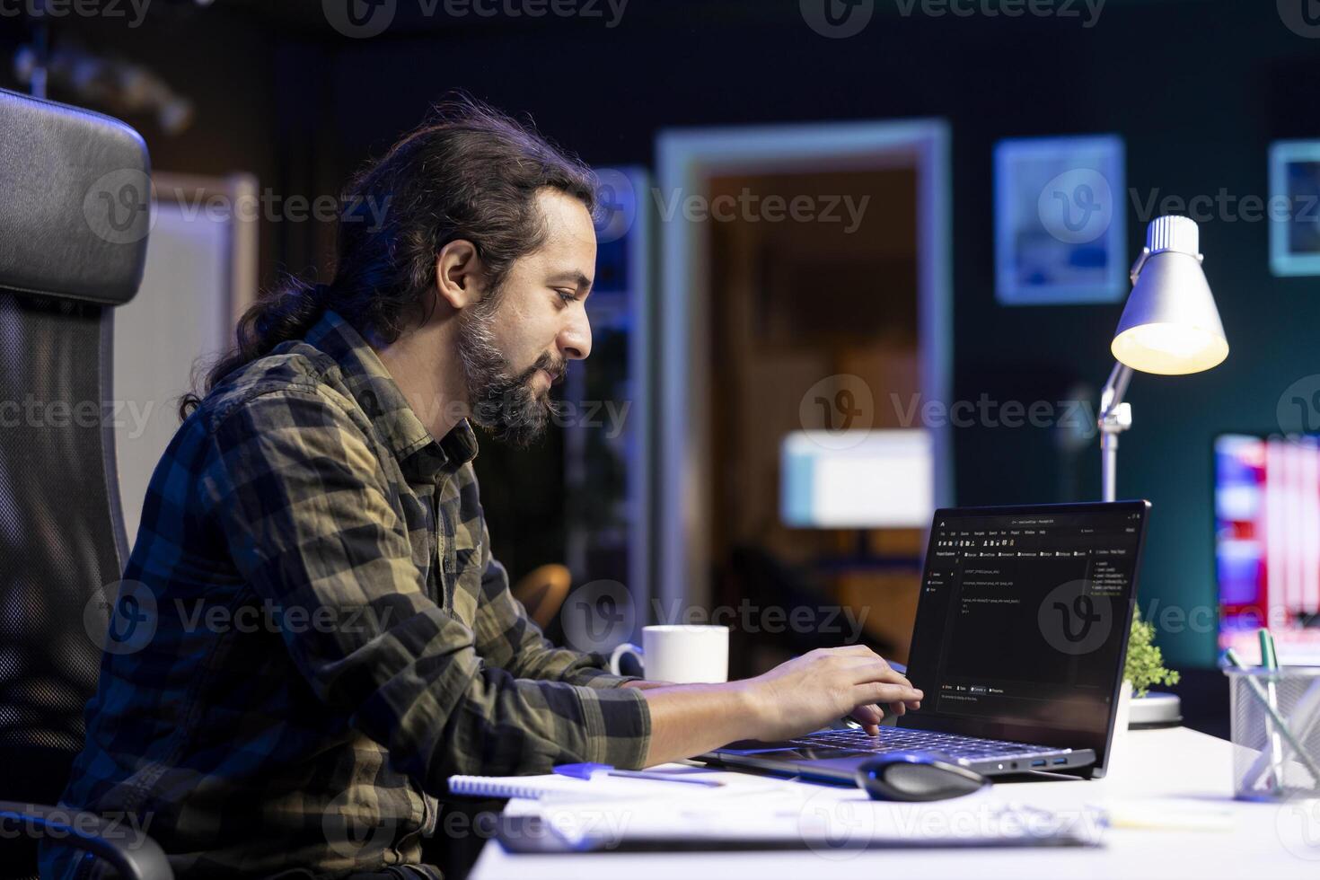 Male programmer works on his portable computer, managing the database and monitoring network for cyber security. Young man sitting at desk and using digital laptop for coding. photo