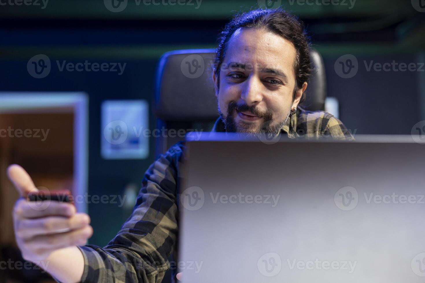 Smiling male freelancer doing internet banking on his laptop, showcasing modern trend of remote work and financial management. Positive guy grasps debit card for online purchases. photo