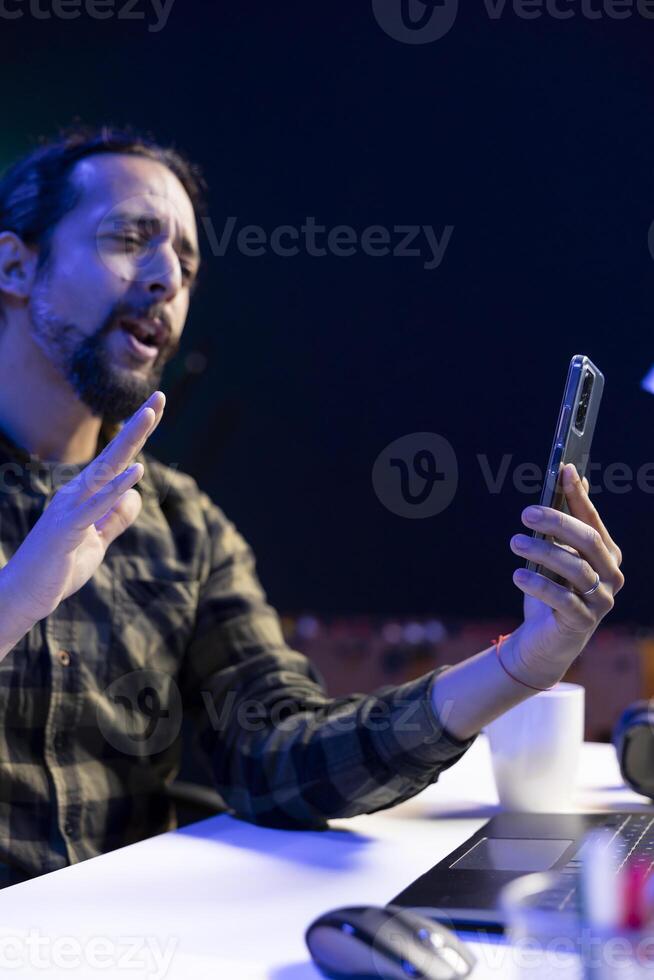 Side view of male university student utilizing his mobile device to conduct a call conversation. Youthful man using hand gestures in virtual meeting with his colleagues through his smartphone. photo