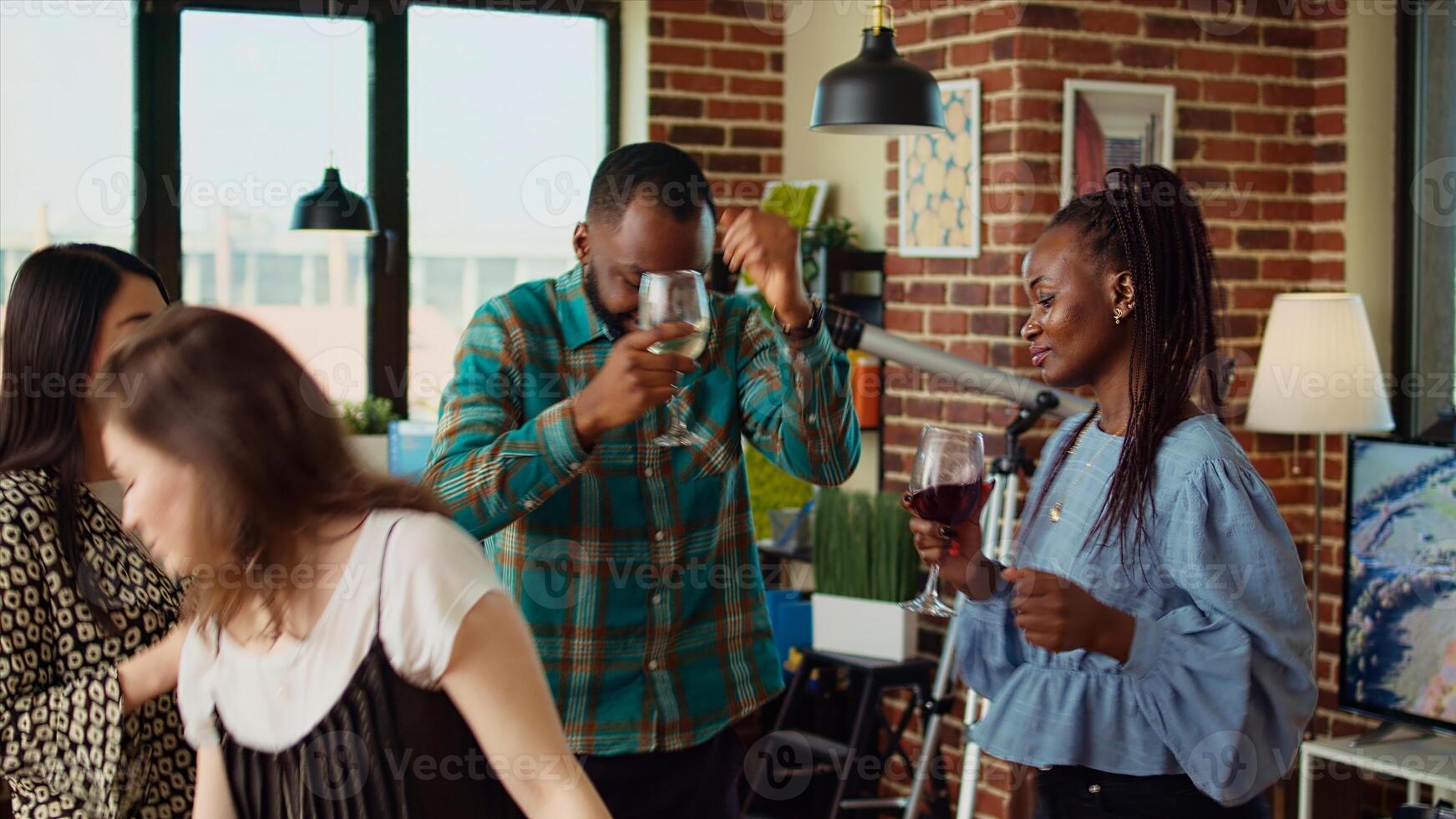 Multiracial school colleagues organizing apartment party, enthusiastically dancing to electronic music in brick wall home. Mates enjoying time spent together, busting into animated dance moves photo