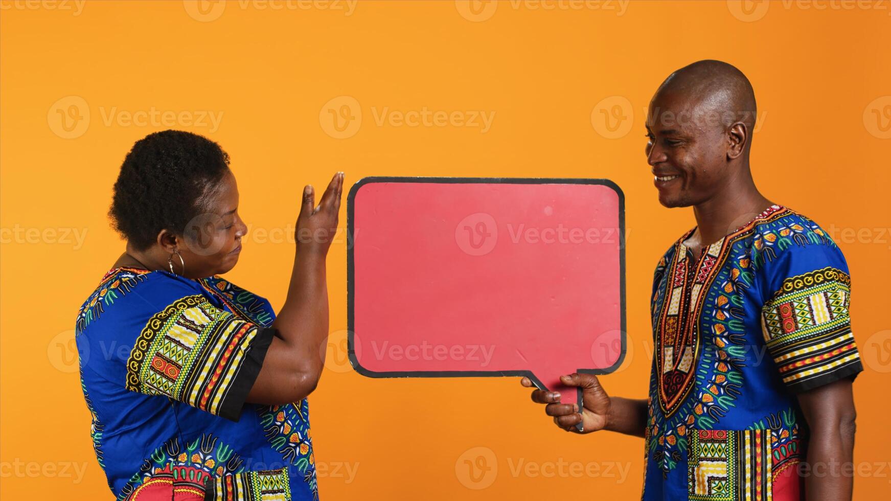 Married ethnic people pointing at red speech bubble icon made from cardboard for web promotions and advertisements. Young man and woman promoting something with isolated billboard sign. photo