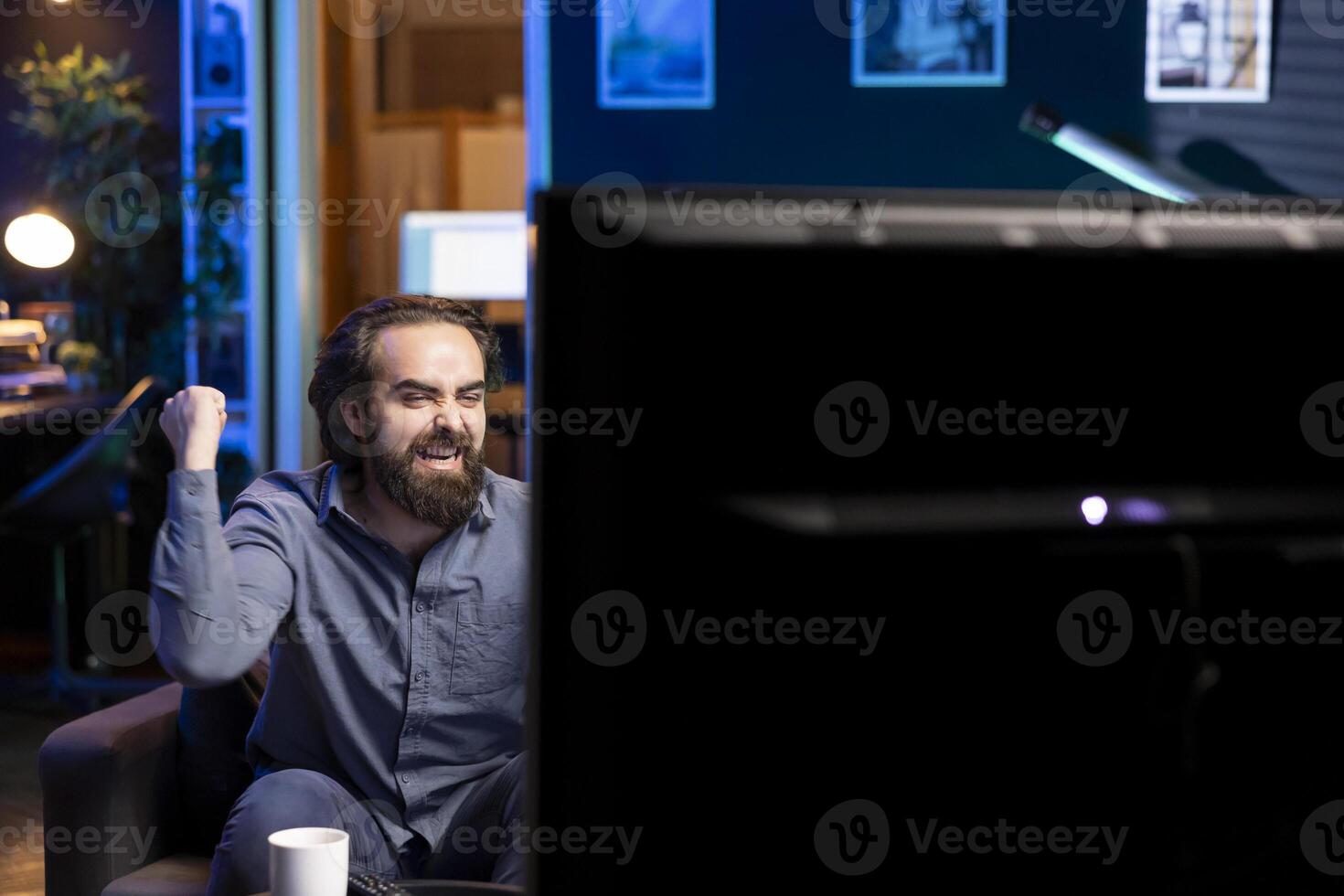 Ecstatic sports fan watching live match broadcast sitting on couch in apartment, celebrating favorite team win. Overjoyed man relishing about own country victory in world cup football competition photo