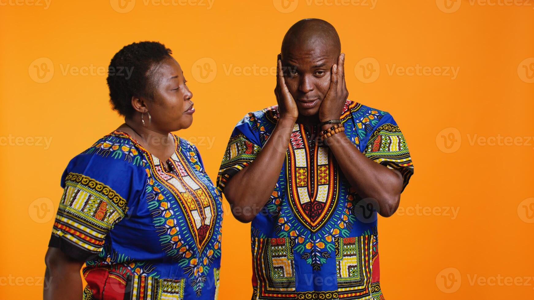 African american woman screaming at her boyfriend and starting argument in front of camera, yelling and causing fight. Young man feeling tired of conflict is covering his ears to ignore his wife. photo