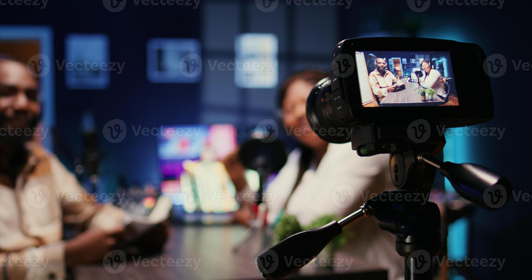 Focus on camera recording man on podcast in blurry background talking with guest during marathon stream for humanitarian cause. Close up of professional gear filming host during internet show photo