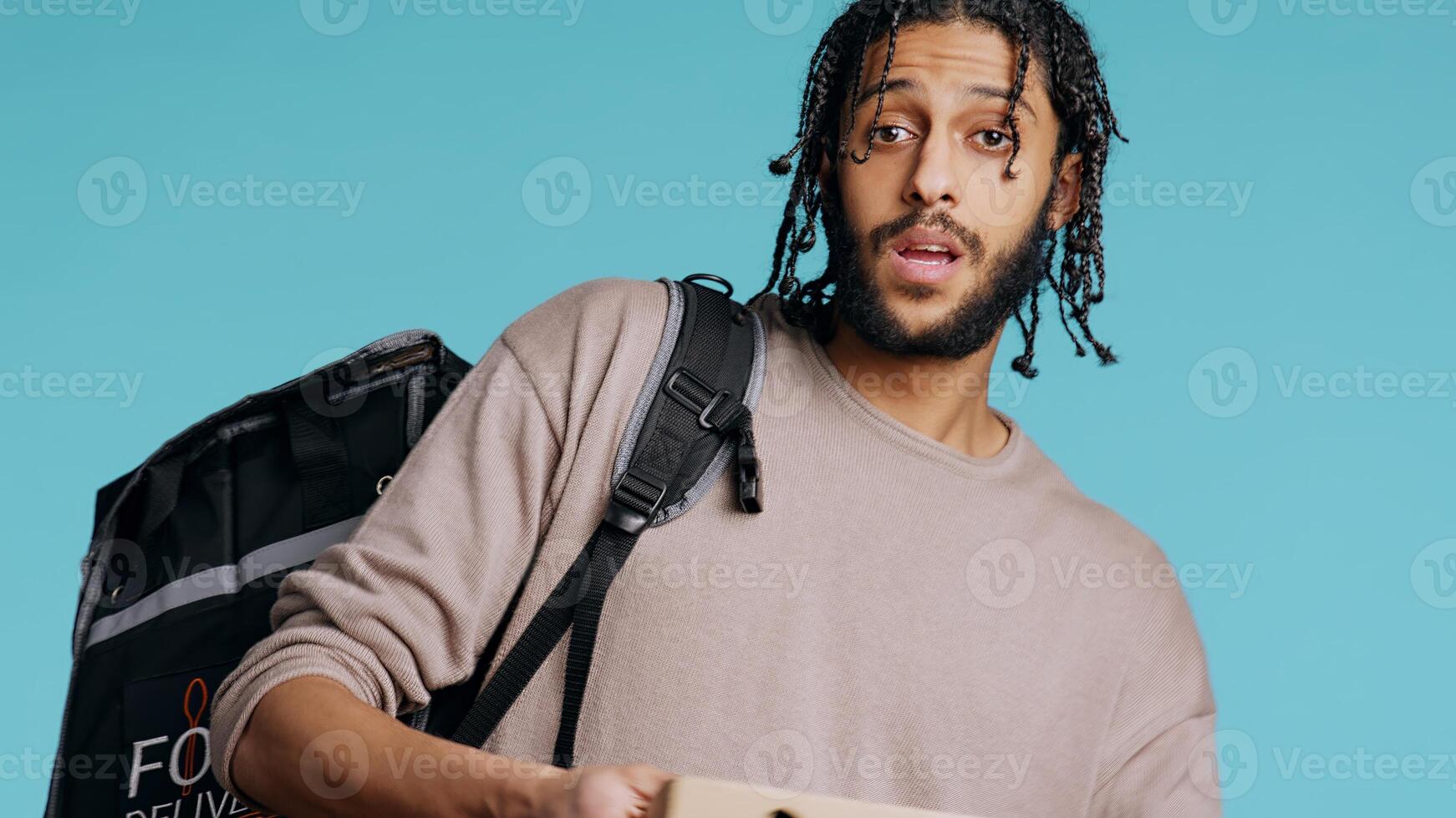 Portrait of BIPOC courier delivering pizza order to client. Delivery part time worker using thermal backpack to store food and bring it to customer, isolated over studio background, camera B photo