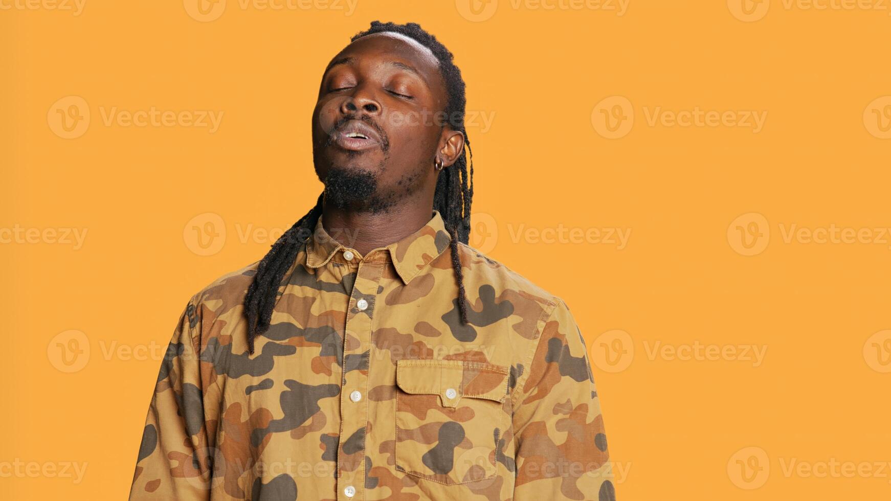 Male model inhaling and exhaling in studio, showing breathing exercises for wellbeing over orange background. Young athletic adult taking breaths and relaxing on camera. Handheld shot. photo