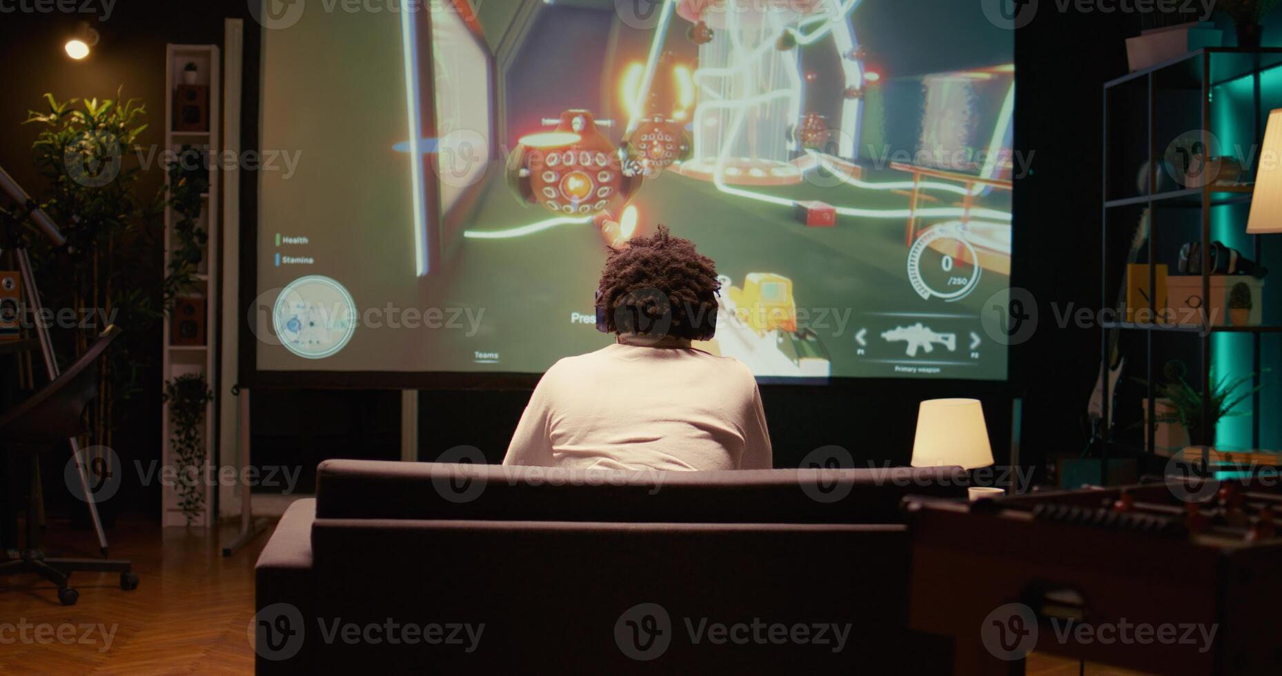 Man watching gameplay footage of videogame competition on gigantic smart TV, relaxing on couch. BIPOC gamer in home theatre following gaming tournament on television set, zoom out shot photo