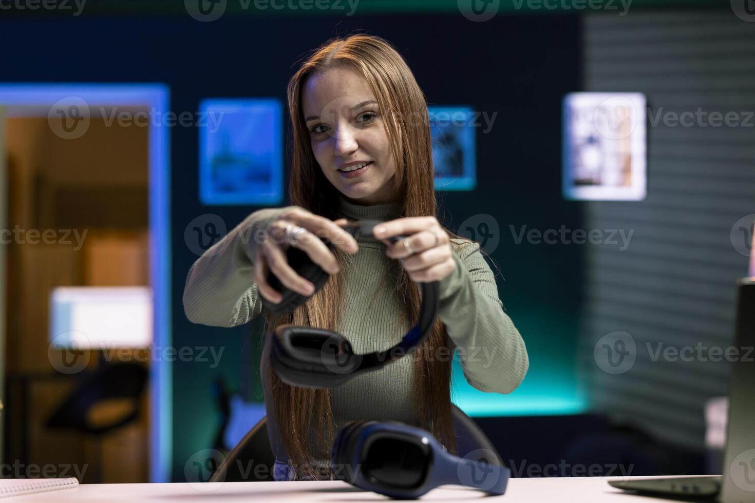 Gen Z online show host holding pair of expensive headphones in hands, doing giveaway for loyal viewers from home studio. Young influencer hosting online contest for fans with audio tech as prize photo