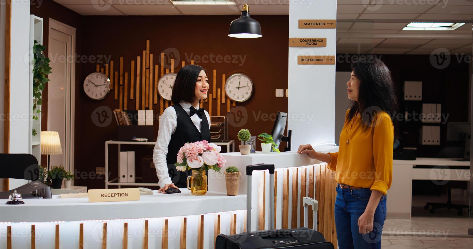 Receptionist welcoming asian woman at five star resort, asking about booking details to fill in registration forms. Front desk staff providing great services for client, presenting hotel amenities. photo