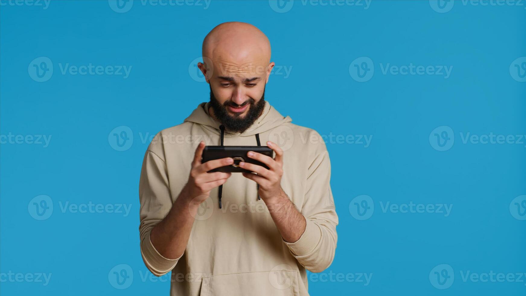 Joyful muslim man playing mobile games in studio, enjoying online competition using smartphone app. Arabic gamer having fun with roleplaying challenge contest. Camera 1. photo