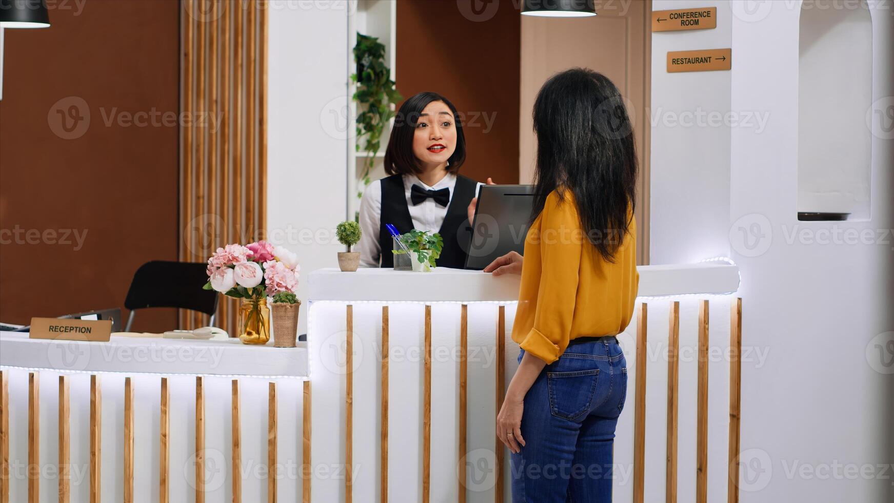 Asian worker doing check in procedure for new visitor at five star hotel, looking for online reservation and ensuring pleasant stay at holiday resort. Client asking for leisure facilities included. photo