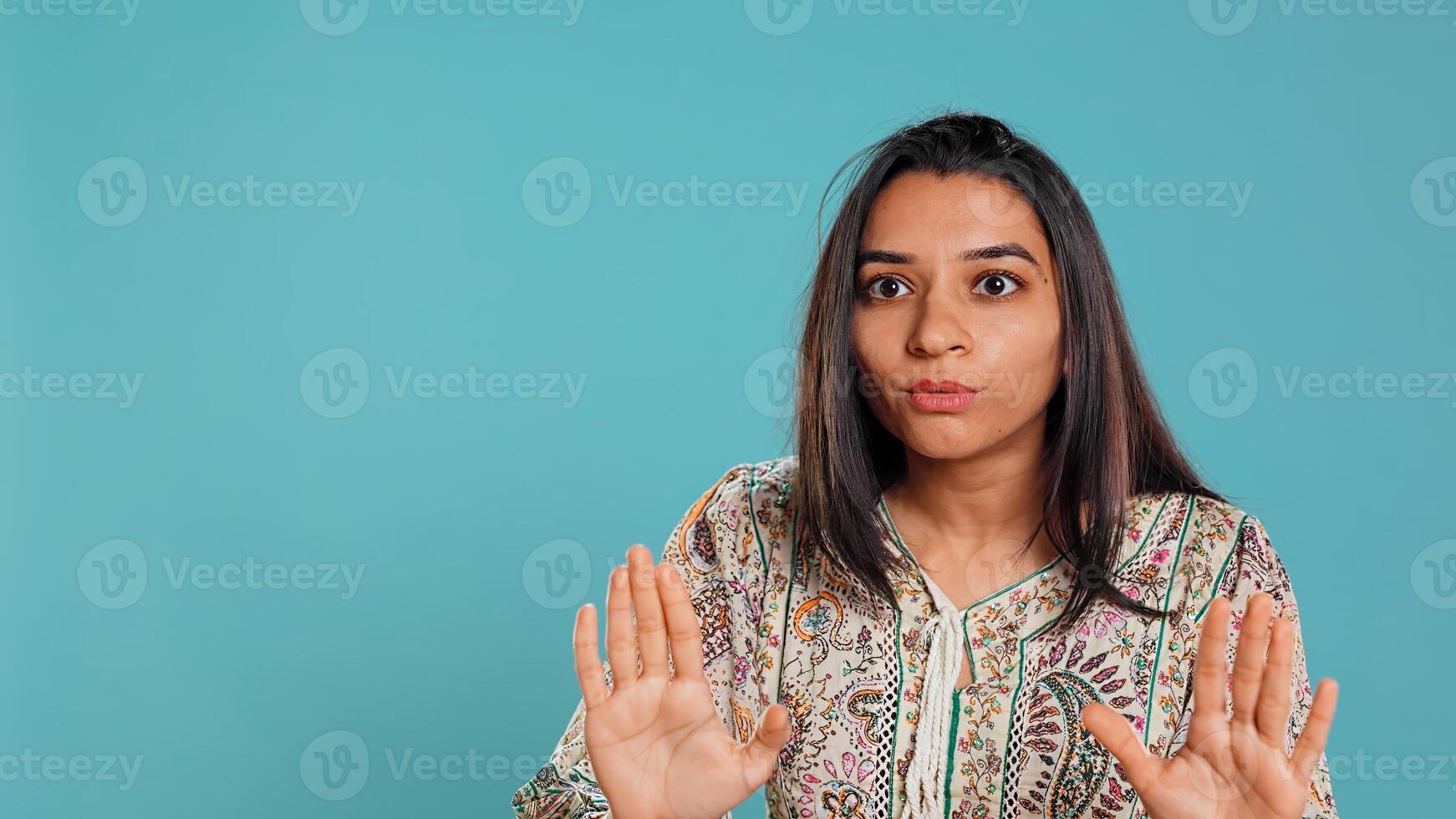 Stern indian woman doing stop hand gesture sign, complaining. Authoritative person doing firm halt sign gesturing, wishing to end concept, isolated over studio background, camera B photo