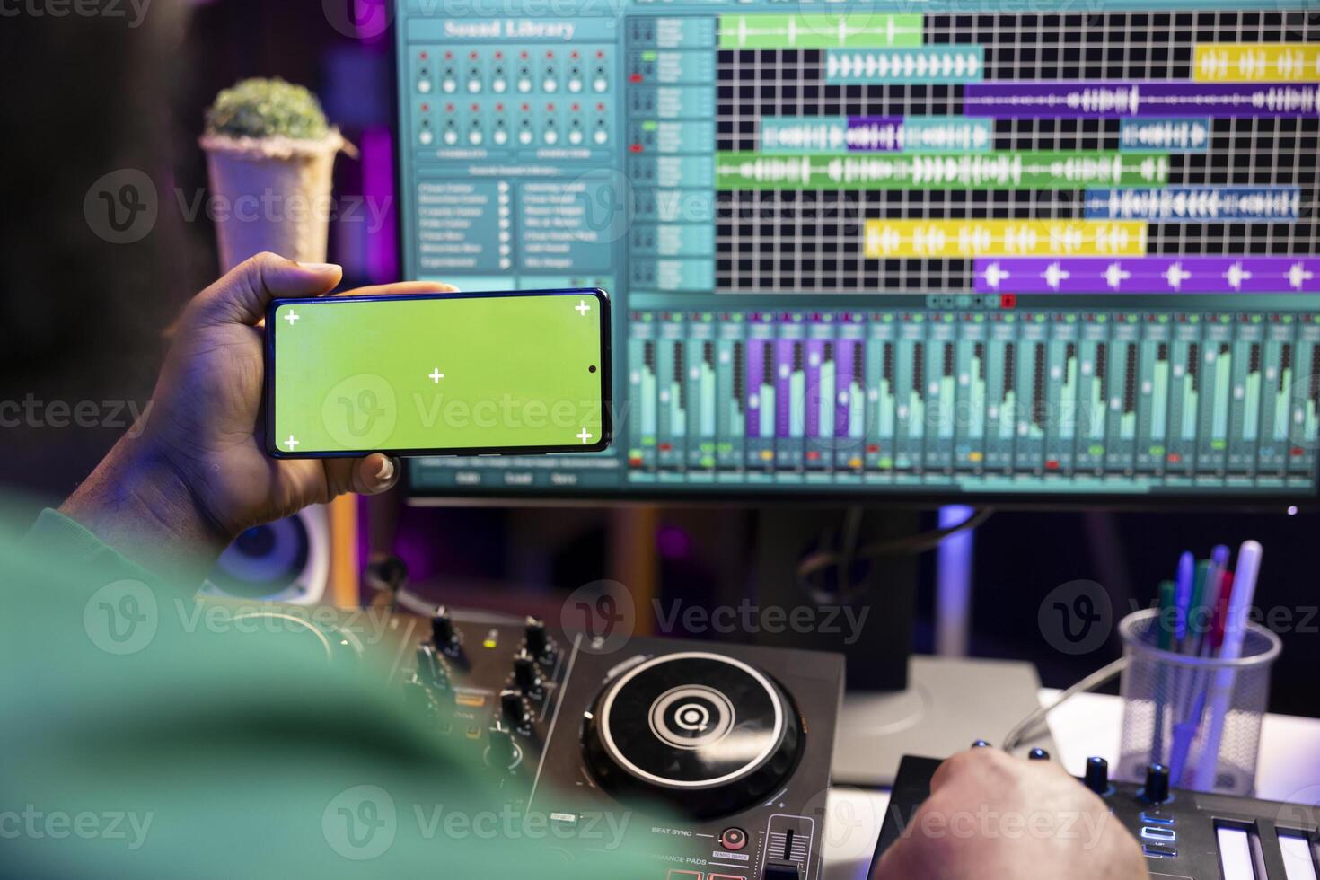 Music producer operating on daw software in home studio and using an isolated display on smartphone, working on new songs. Professional technician adjusting volume levels with mixing console. photo