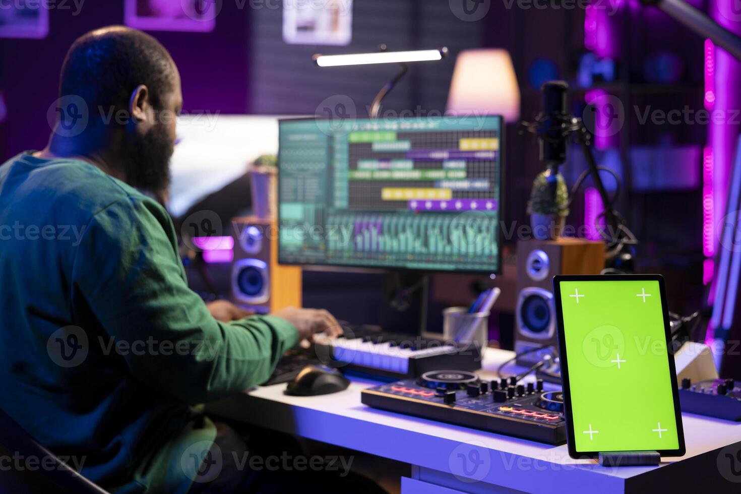 Composer editing his audio files and recordings on daw software, sitting next to a greenscreen display. Skilled sound technician uses mixing and mastering gear to produce new material. photo