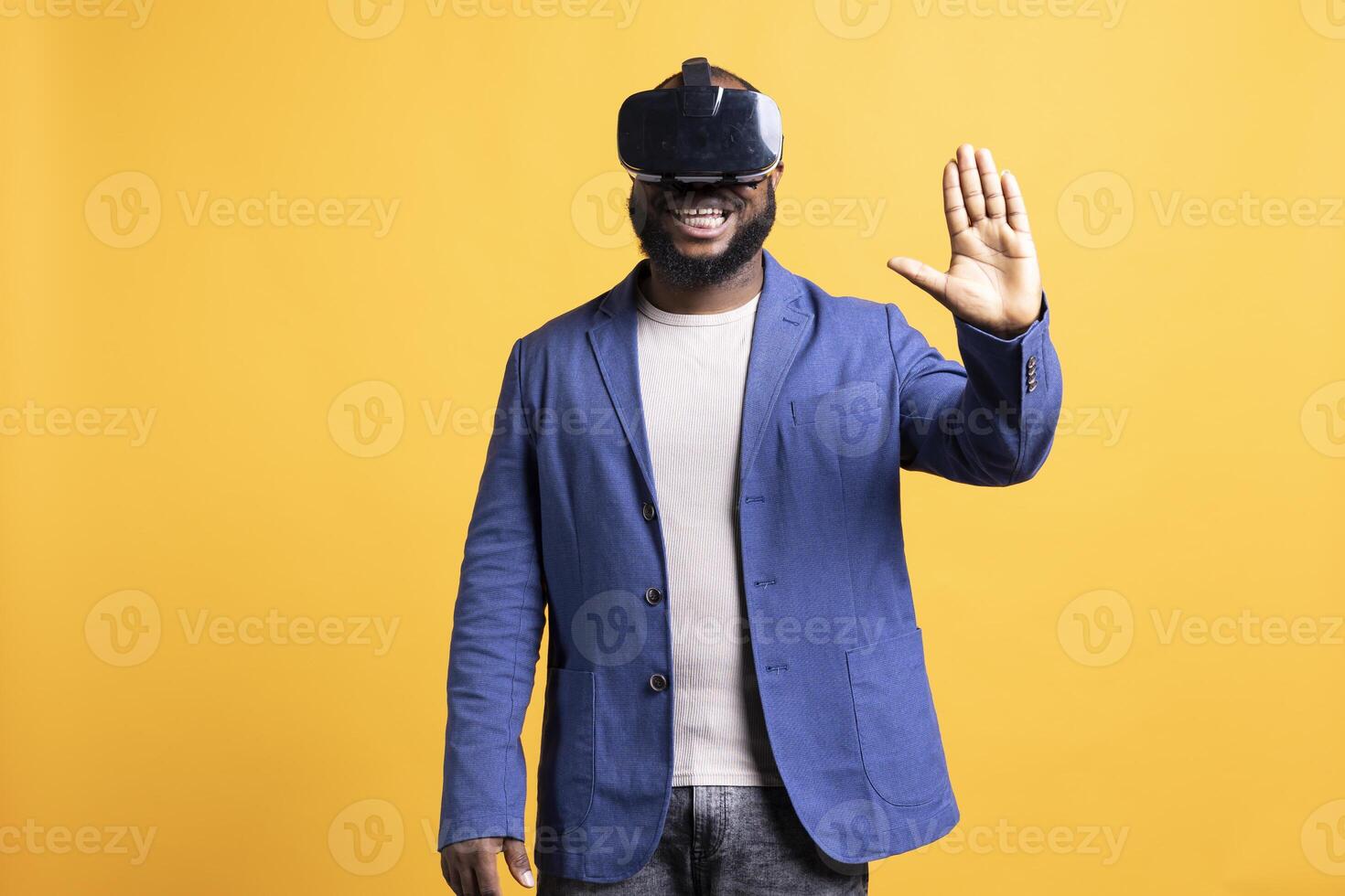 Smiling man wearing virtual reality headset, interacting with interface. Upbeat BIPOC person using high tech futuristic modern VR gadget, isolated over yellow studio background photo