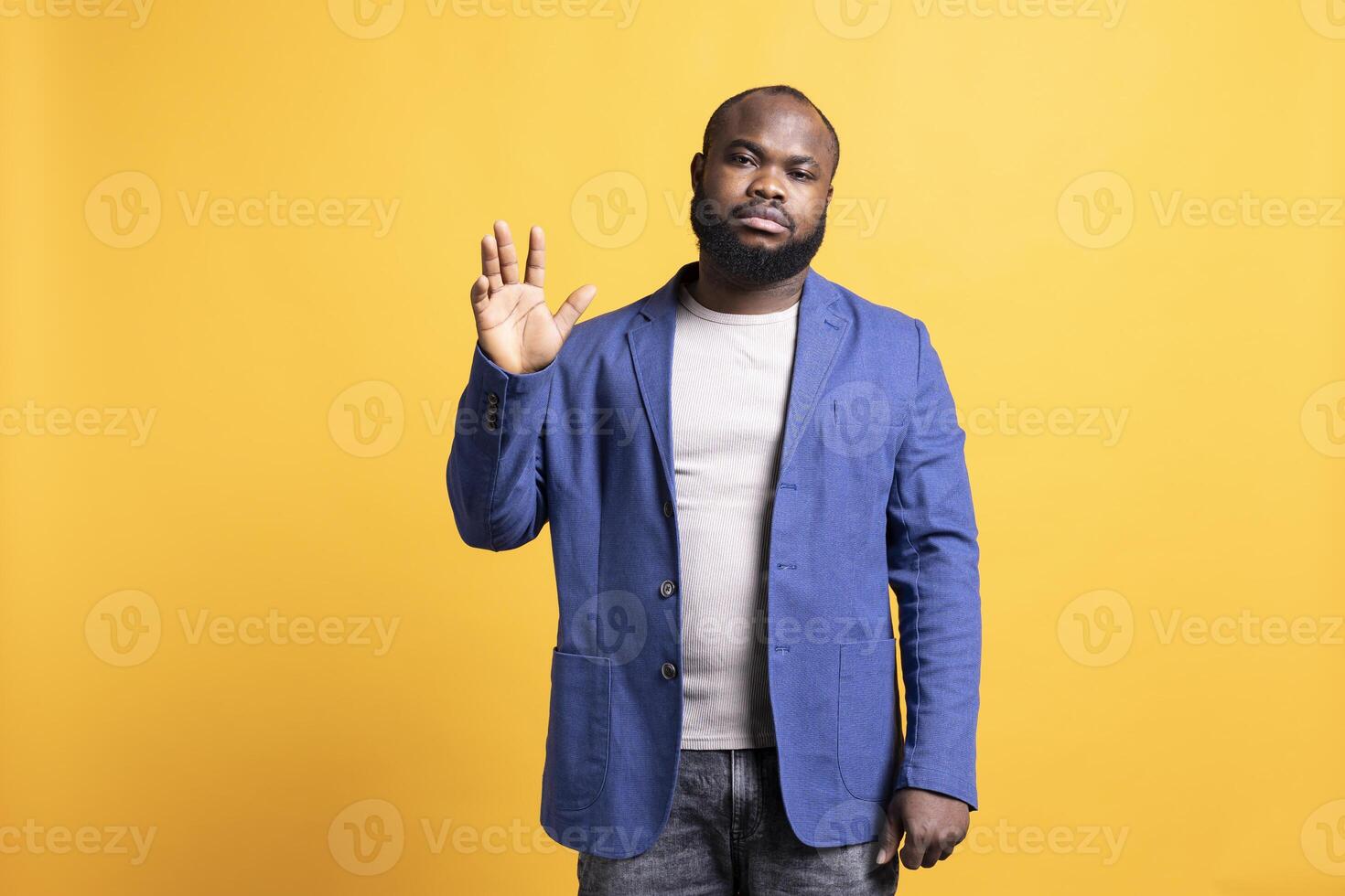 African american man reluctantly doing salutation hand gesture. Portrait of emotionless BIPOC person raising arm to greet someone, gesturing, isolated over yellow studio background photo