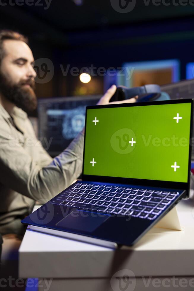Programmer updating artificial intelligence algorithm using green screen laptop, making it become sentient. IT specialist programming self aware AI with mockup notebook photo