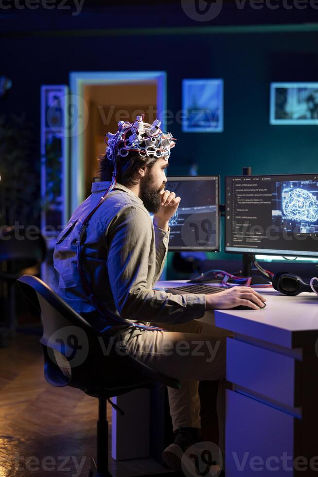 Man puts EEG headset on to transfer mind into computer virtual world, becoming one with AI superintelligence. Engineer using futuristic neuroscientific technology to transfer consciousness photo