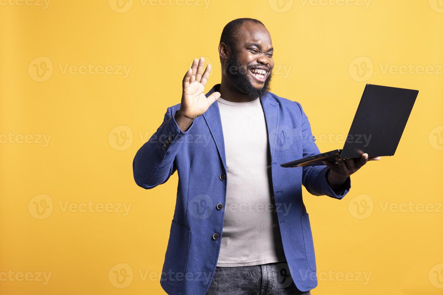 Joyful african american man greeting coworkers during teleconference meeting, isolated over studio background. Happy worker waving hand, saluting colleagues during internet call photo