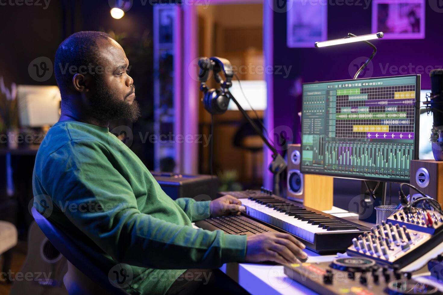 African american artist composing a new soundtrack for a project, using professional production software in his home studio. Skilled creative singer producing music and adding sound effects. photo