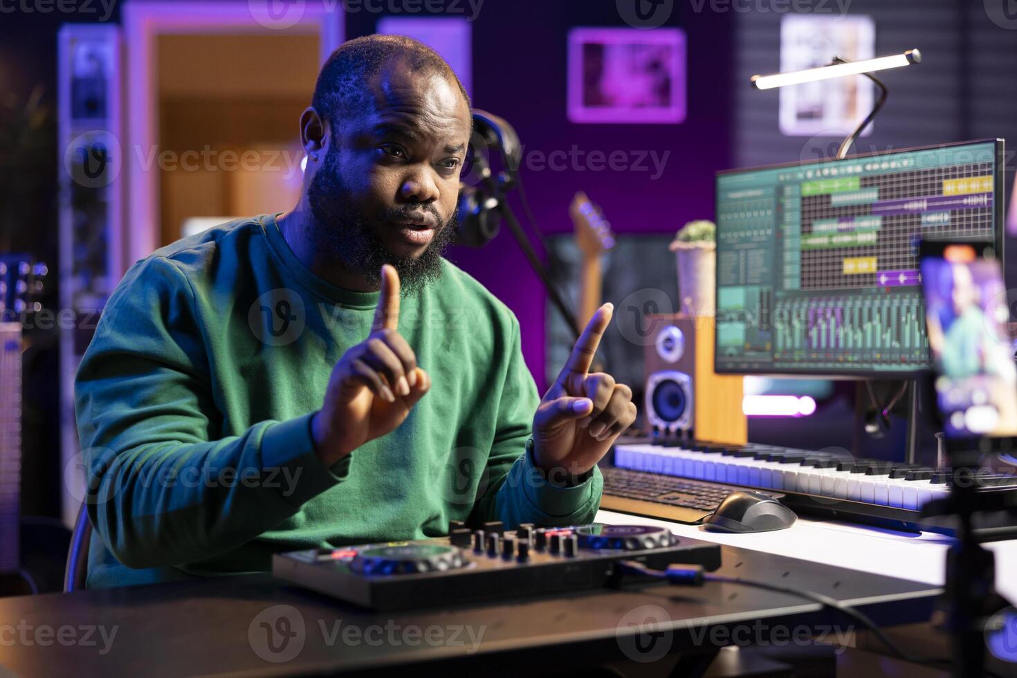 Young producer teaching people to use a mixing console during online lessons, recording himself with a smartphone. Sound engineer hosting a master class to teach editing in post production. photo