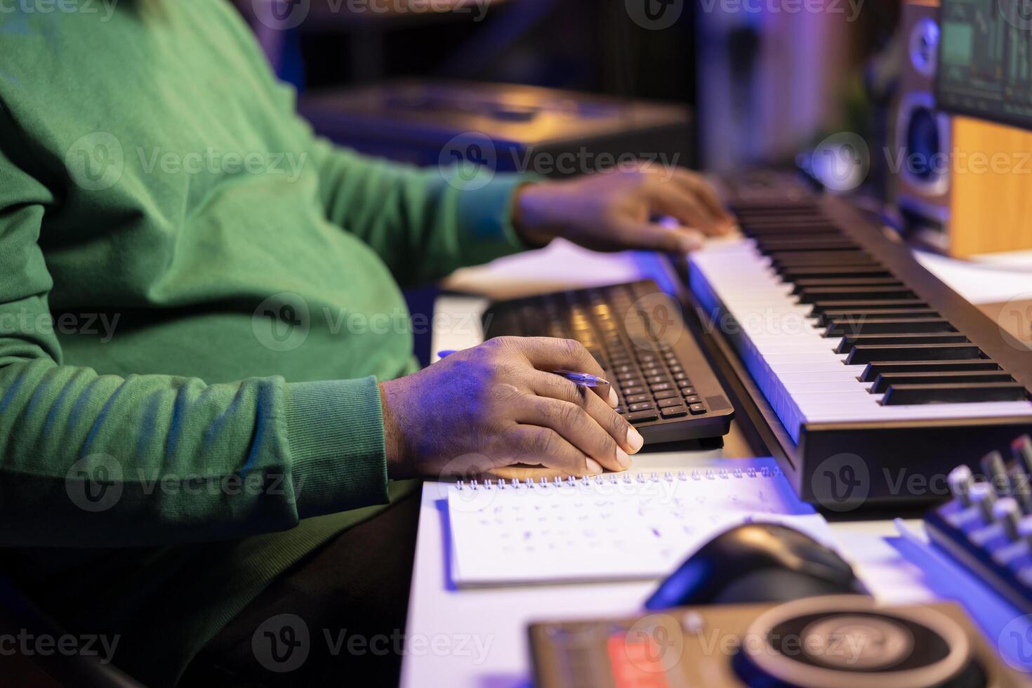 In his home studio, songwriter writes down lines and melodic elements to create new tunes. Using digital audio workstation software, composing and recording songs in post production. photo
