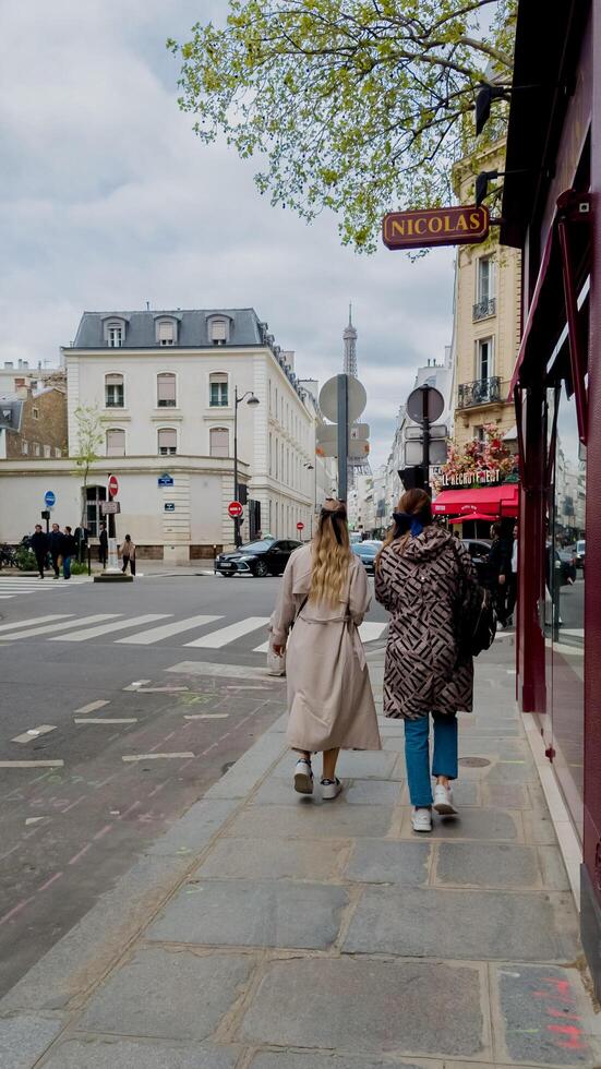 Two women casually strolling along a Parisian street with the Eiffel Tower in the distance, photographed in Paris, France, on April 14th, 2024, perfect for travel and friendship themes photo