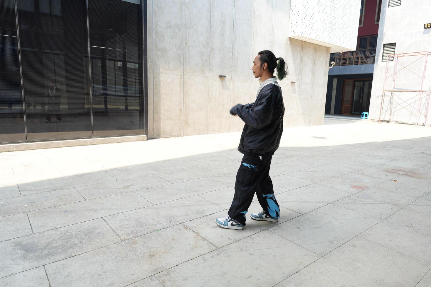 ASian man is dancing in hip hop style at outdoor space. Professional solo dancer is performing in public area. photo