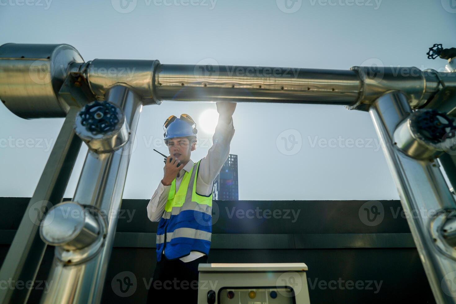 Urban rooftop scene showing a young engineer with a radio, inspecting and adjusting equipment in a sunny city environment. Safety and precision at work. photo