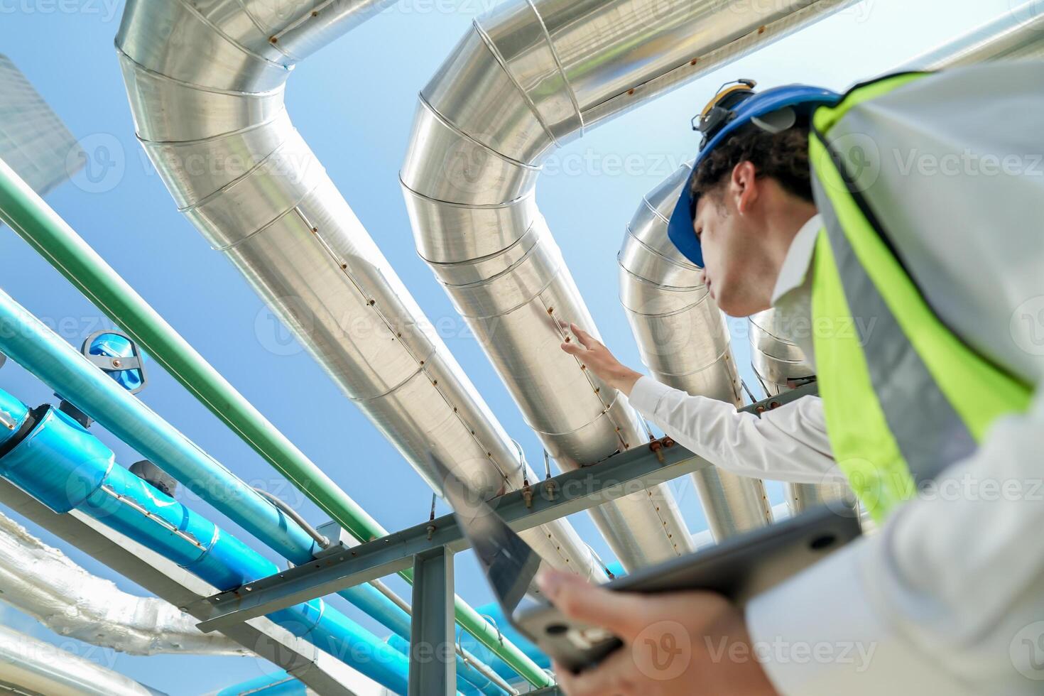 Industrial engineer adjusting pipeline valve with radio communication on construction site. Engineer on urban construction site using radio to coordinate with team on a sunny industrial rooftop. photo
